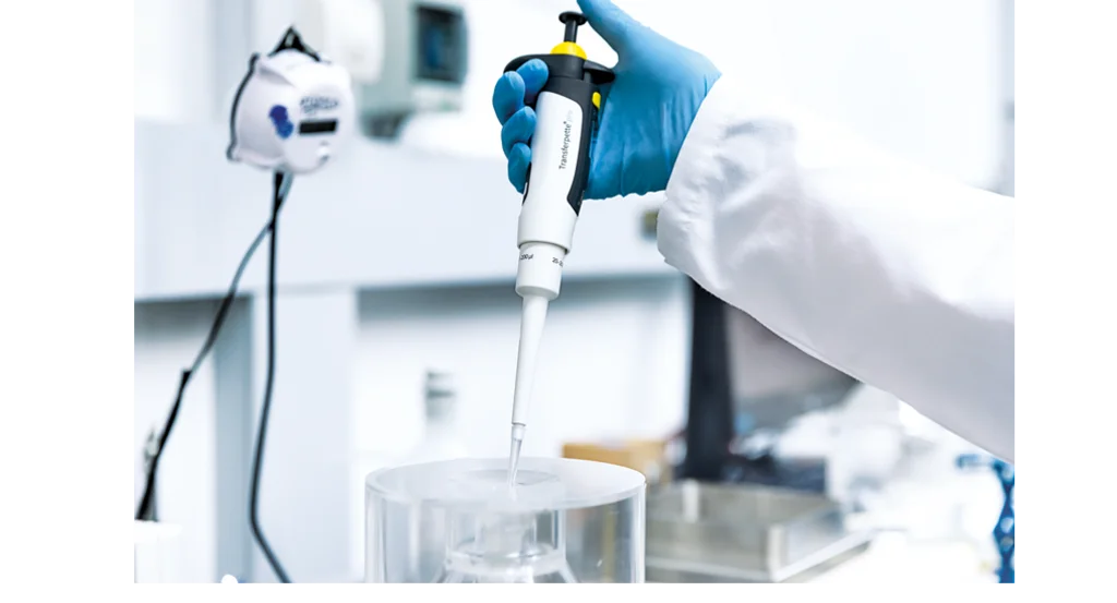 Gloved hand operating a Transferpette micropipette during a laboratory volume check, showing equipment used for pipette monitoring and maintenance.