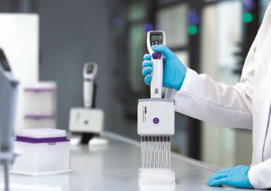 Person mit blauen Handschuhen nutzt eine elektronische 8‑Kanal‑Pipette von BRAND zum Befüllen einer Well‑Platte